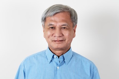 portrait of attractive senior asian man smiling and looking at camera in studio with white isolated background feeling positive grandpa. headshot of mature older chinese man or father concept.