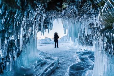 travelling in winter, a man standing on frozen lake baikal with ice cave in irkutsk siberia, russia