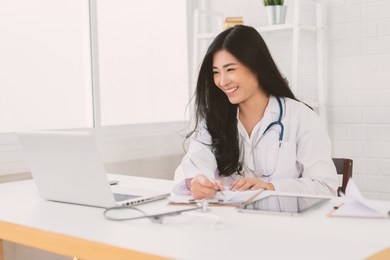 asian female doctor sitting at hospital office desk giving all patient convenience online service advice and smiling write a prescription to order medical, health care and preventing disease concept.