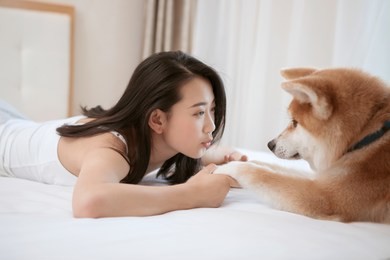 young asian woman lying on bed, playing with pet dog.