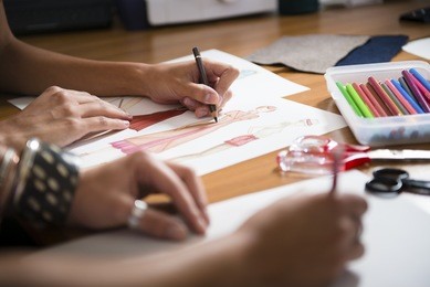 two young women working as fashion designers and drawing sketches for clothes in atelier. cropped view