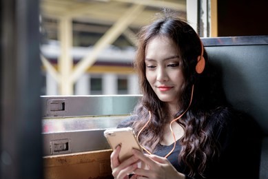 asian woman traveler has listening music with phone and orange headphone inside the train.