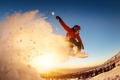 snowboarder jumps or flies against sunset light with snow dust