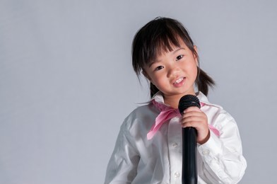 5 years old of happy emotional little asian girl holding microphone and singing on white background. funny children look and smile while holding mic. dream career with learning of children concept.
