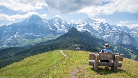 mountaineer resting at wooden bench, enjoying the view to eiger, monch and jungfrau. famous peaks at bernese oberland, swiss alps