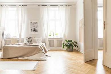 spacious and bright bedroom interior with beige decorations, hardwood floor and a book on the window sill seat