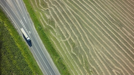 aerial top view of white truck with cargo semi trailer moving on road in direction f loading warehouse area.