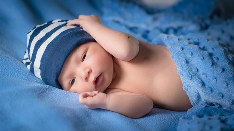 newborn baby boy with blue beanie lies awake under blue blankets