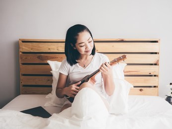 asian woman play ukulele on her bed in the morning.