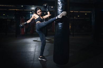 female boxer hitting a huge punching bag at a boxing studio. woman boxer training hard. thai boxer punch kick by punching bag, black bacground