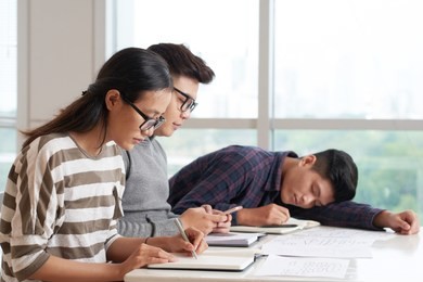 vietnamese college student sleeping in class when his classmates writing in textbook or texting