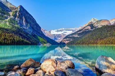lake louise in banff national park with its glacier-fed turquoise lakes and mount victoria glacier in the background. visitors paddling red canoes in the distance.