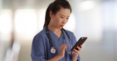 serious millennial doctor on break reading texts with smartphone inside hospital