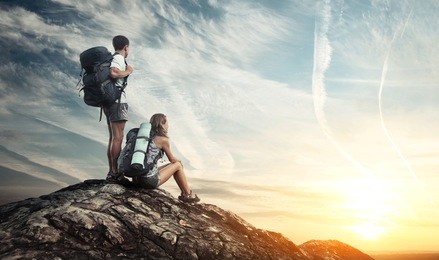 two tourists with backpacks enjoying sunset on top of a mountain