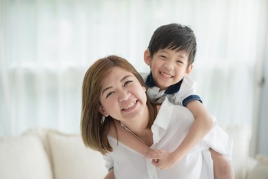 asian child on a piggy back ride with his mother at home
