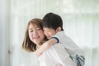 asian child on a piggy back ride with his mother at home