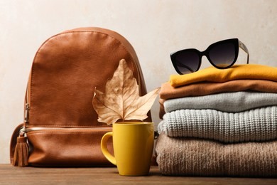 backpack and warm clothes on wooden table on neutral background. concept autumn clothes.