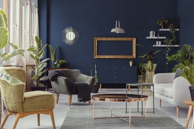 copper table between armchairs and sofa in blue living room interior with mockup and mirror. real photo
