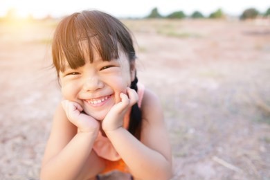 asian child poor or kid girl smile with laugh and happy fun because come back home to country and wear traditional top or sleeveless shirt sit on arid soil for agriculture at home and warm sunlight