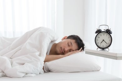 young asian handsome man sleeping in his bedroom. boy sleeping with alarm clock in foreground. the time is half pass 7 am. wake up in morning of working day concept.