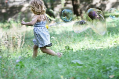 young cute child girl blowing big soap bubbles