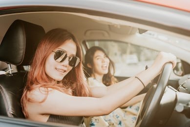 two happy asian girl best friends laughing and smiling in car during a road trip to vacation