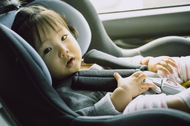 asian 9 month toddler baby sitting on car seat with fasten seat belt and looking curious.