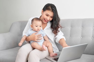 young asian mother sitting on sofa at home with computer and her daugher