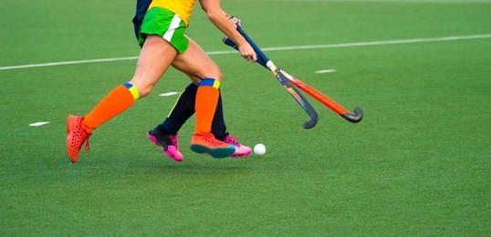 close up of two field hockey players, challenging eachother for the control and posession of the ball during an intense, competitive match on professional level