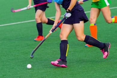 three women battle for control of ball during field hockey game