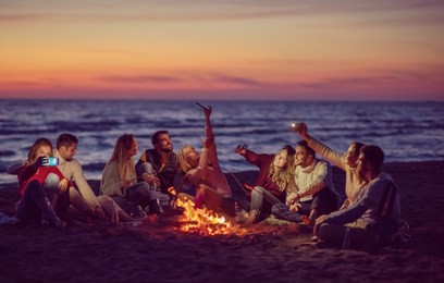 a group of friends using cell phones around the bonfire during autumn beach party drinking beer and having fun filter