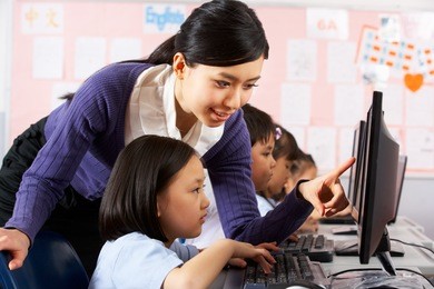 teacher helping student during computer class in chinese school classroom