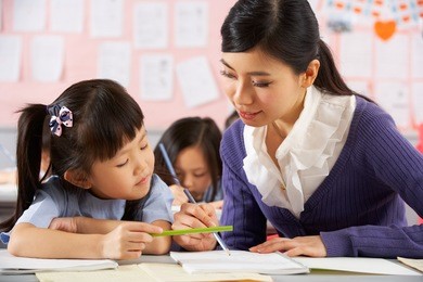 teacher helping student working at desk in chinese school classroom
