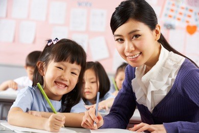 teacher helping student working at desk in chinese school classroom