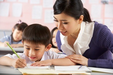 teacher helping student working at desk in chinese school classroom
