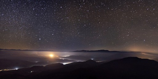 starry sky over foggy mountains panorama with city lights below