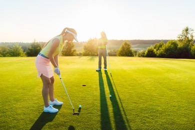 full length side view of a female golf player ready to hit the ball into the cup, under the guidance of a qualified instructor during class outdoors at a modern country club