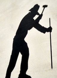 shadow of a person preparing to hammer a iron stake with a sledge hammer reflected on a cement slab