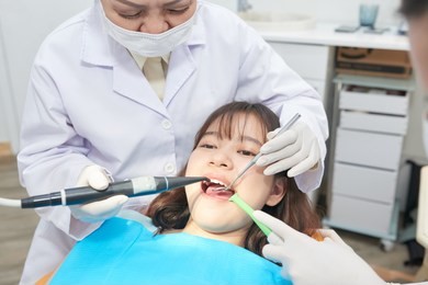 crop doctor and assistant taking care of young asian girl in dental chair working in team