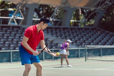 side view of an asian tennis player ready to serve at the beginning of a doubles mixed match on a professional tennis court