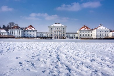 germany, bavaria, munich, nymphenburg palace: panorama view of winter scene with main building entrance of the famous castle, white snow, blue icy sky in the bavarian capital.