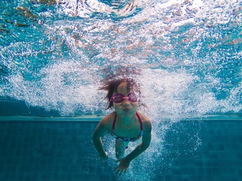 cheerful asian little girl diving and swimming in pool on summer vacation.