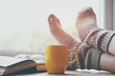 woman resting keeping legs in warm socks on table with morning coffee and reading book