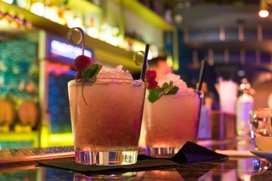 two alcoholic cocktails of pink color with raspberries, ice and mint are on bar. neon lighting. the concept of friday's holiday