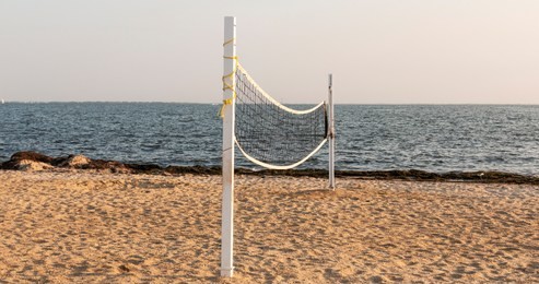 a beach has a volleyball net set up on the sand ready for athletes to come and play by the water.