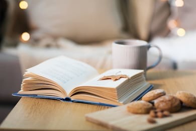 hygge and cozy home concept - book with autumn leaf, cup of tea and oatmeal cookies on wooden table