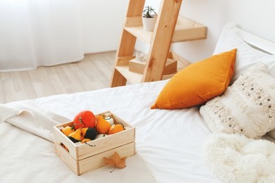 home decor. cozy fall bedroom interior: white wall, wooden rack, bed with white linen, light beige plaid, orange pillows,  wooden box with pumpkins. autumn decoration.
