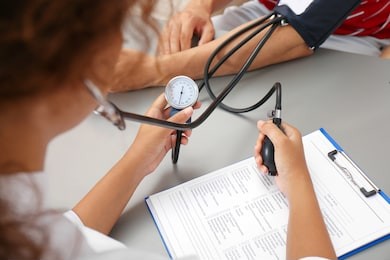 doctor checking patient's blood pressure at table in office, closeup