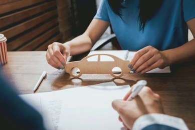 man signing a car insurance policy, the agent is holding the wooden car model. car insurance concept.