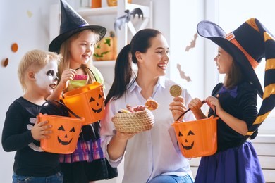 happy family celebrating halloween! young mom treats children with candy. funny kids in carnival costumes.